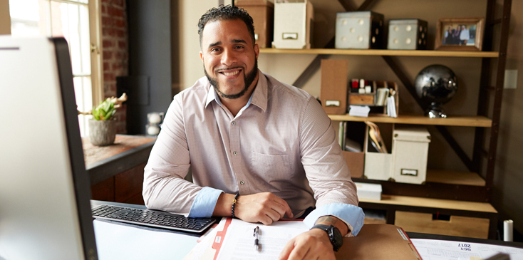 man in a dress shirt sits at a desk and looks past his computer