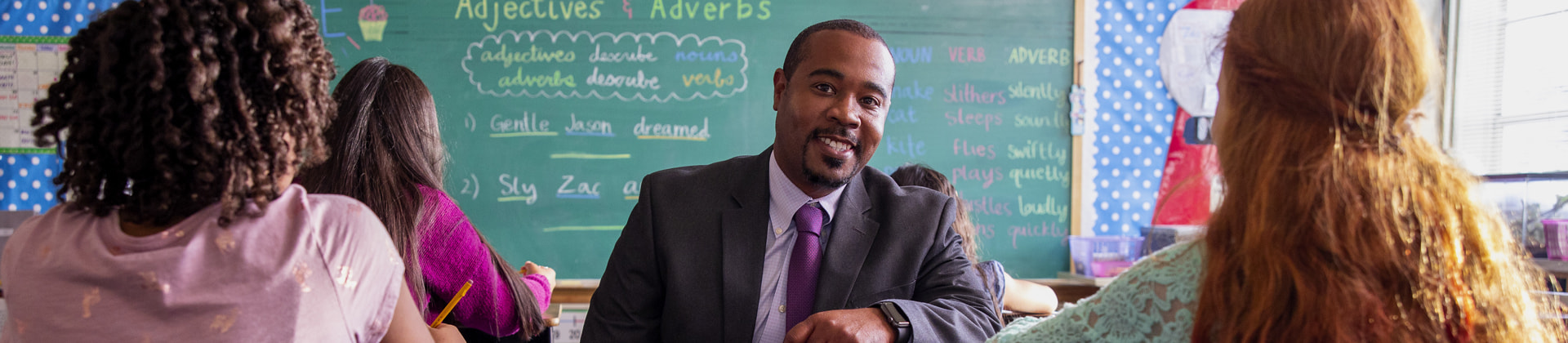 Prince M. sits in a classroom in between children, who are looking the other way toward the chalkboard