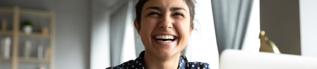 woman at home smiling as she looks above her laptop