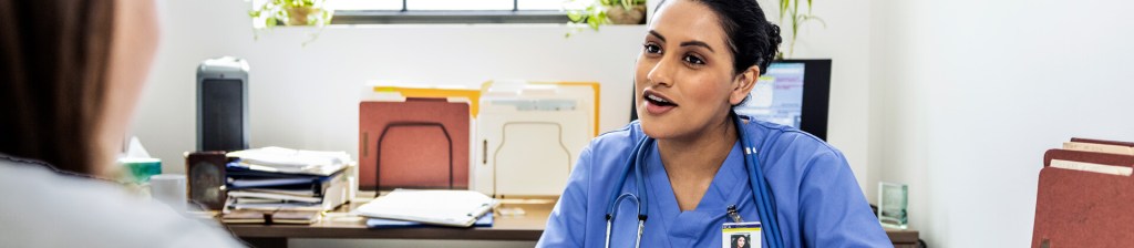 medical professional sitting at desk speaking with person across from her