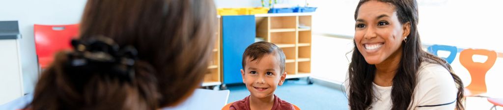 Mother and preschool aged son smiling at teacher in classroom