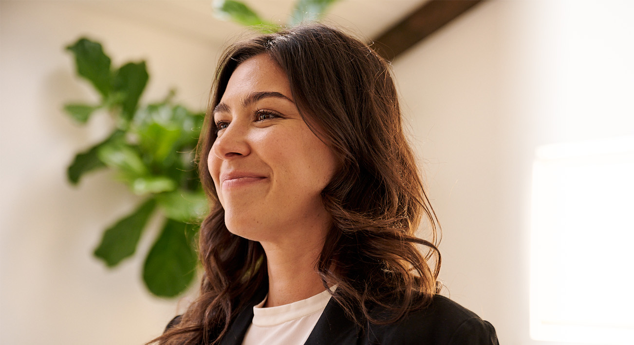 Woman with wavy brown hair smiles at someone out of frame