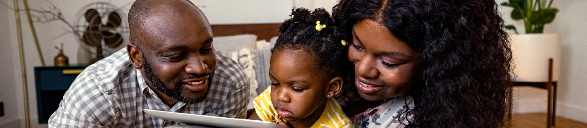 father and mother with toddler child between them looking at tablet