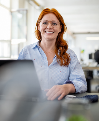 woman with glasses and long hair works on a laptop in an open office