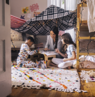 woman plays with two kids in a fort in a child's bedroom