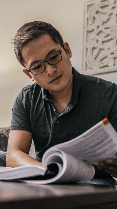 man with glasses reads a textbook