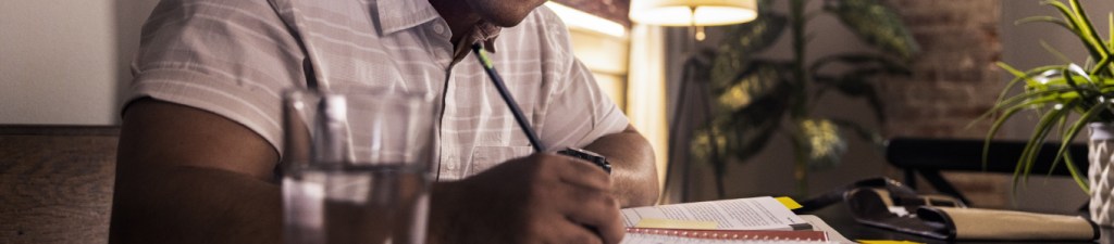 man at desk writing in notebook with textbook opened