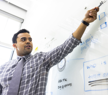 Man in a tie and dress shirt teaches at a whiteboard