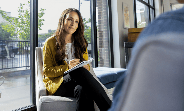 woman with a note book listens to a person out of frame