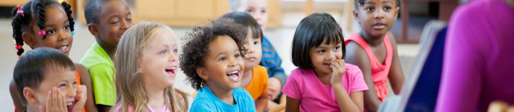 group of preschoolers sitting on floor smiling towards teacher