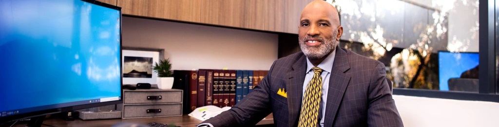 bald man in a suit sitting at a desk next to a computer