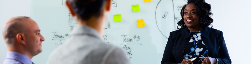 men and women talk in front of a white board filled with facts and figures 