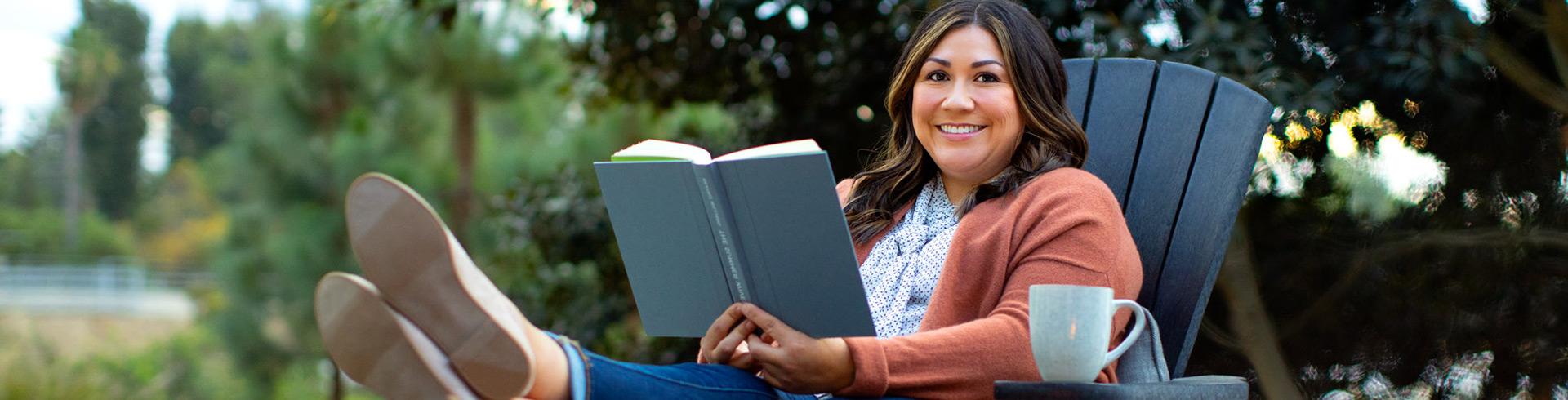 woman sits in an outdoor chair reading a book