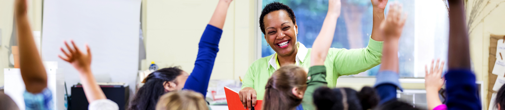 Teacher in classroom with kids raising hands