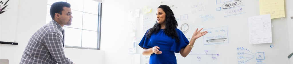 people talking in front of whiteboard with notes written on it