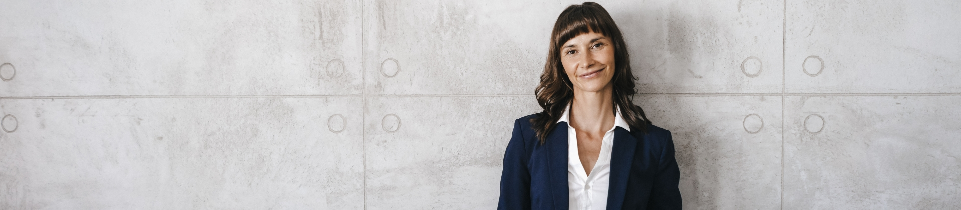 woman stands against a concrete wall in a suit