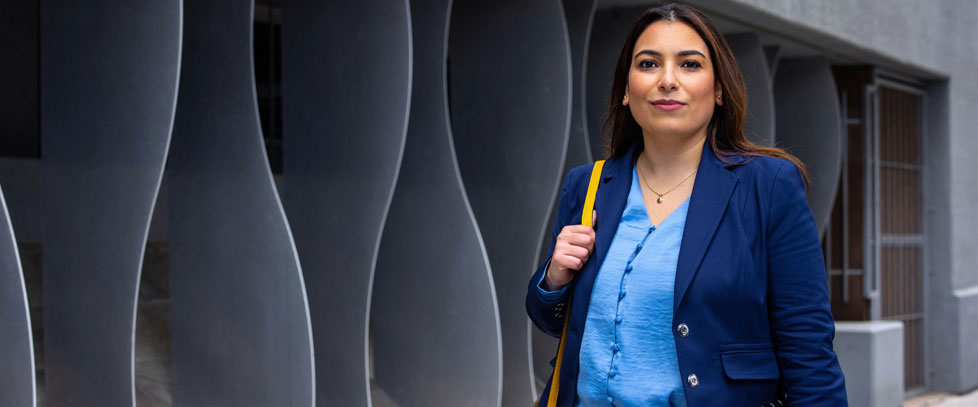 woman in a blazer stands in front of sculptural wavy walls outside