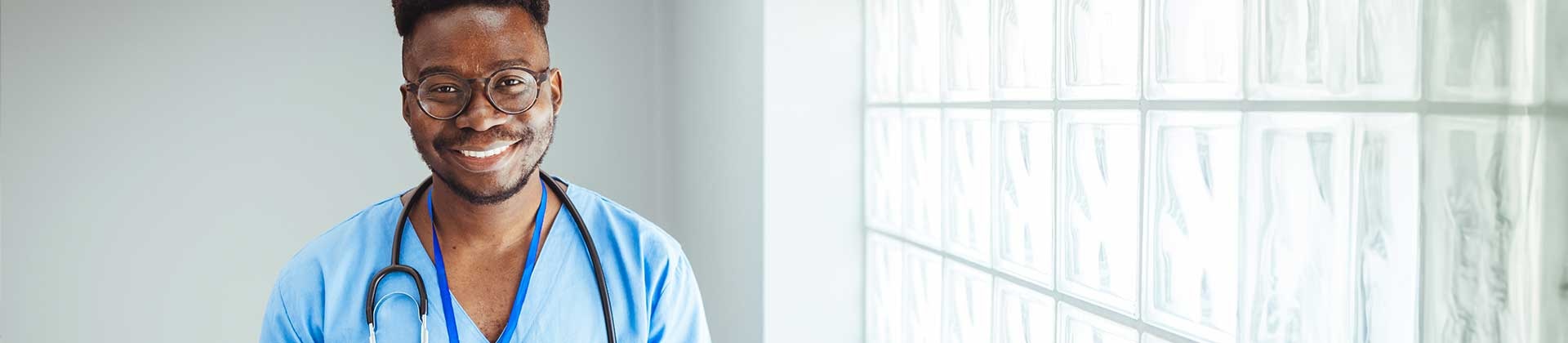 Man in scrubs stands by a window