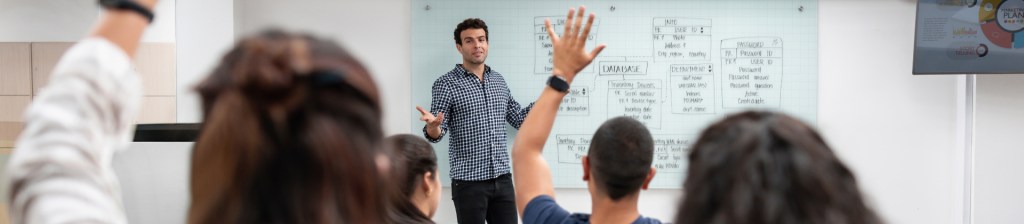 person teaching at white board with students who are raising their hands