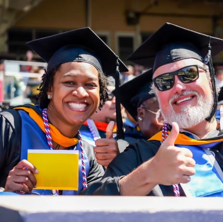 man and woman in graduation cap and gown smiling among other graduating students